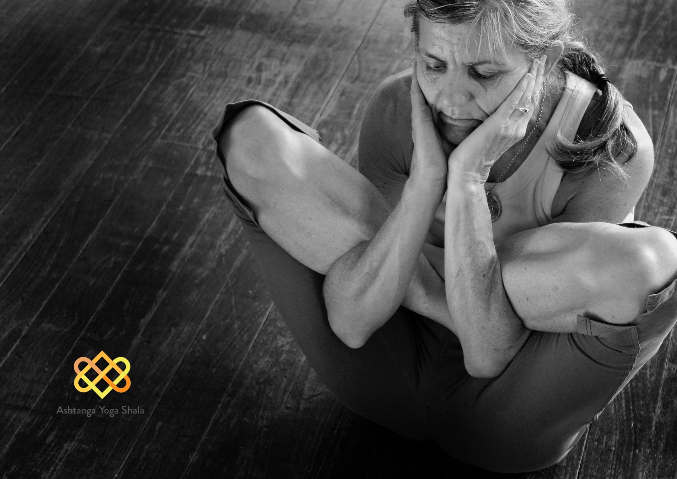Black and white photo of a woman holding a deep forward-folded yoga pose with elbows resting on her knees.