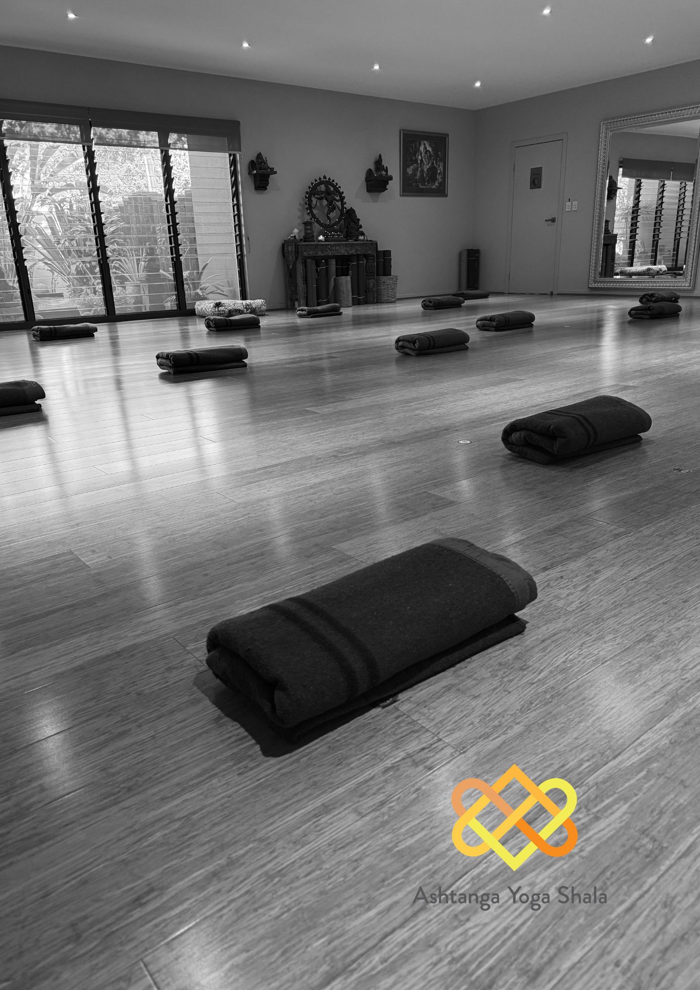 Black and white photo of a yoga studio with neatly folded blankets spaced across the timber floor.