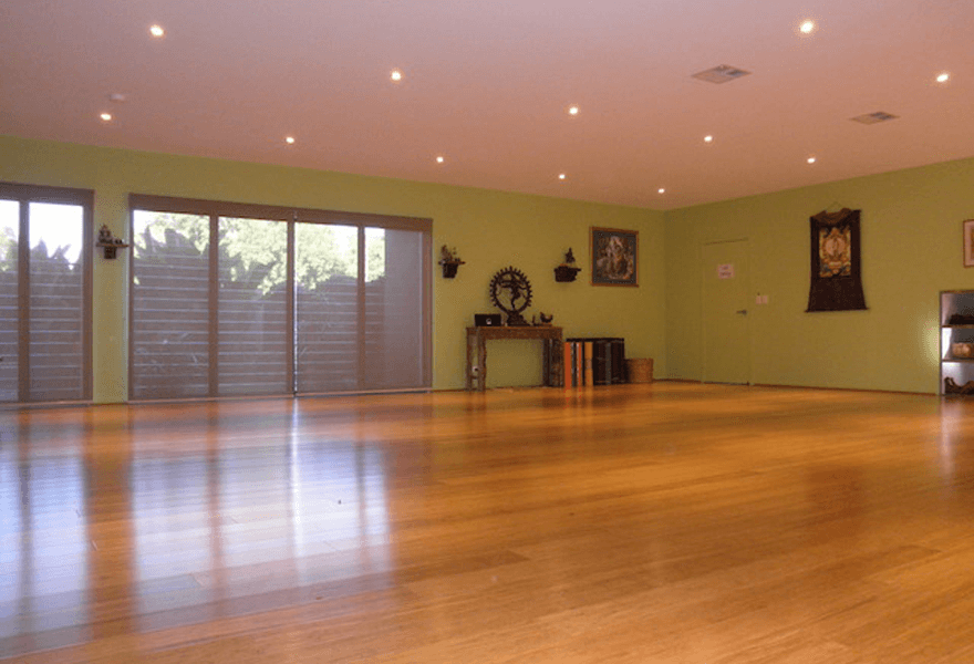Spacious yoga studio with polished timber floors, green walls, soft lighting, and large windows letting in natural light.